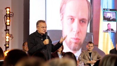 Міський голова Львова Андрій Садовий з мікрофоном у руках спілкується з першим заступником Міністра аграрної політики та продовольства Денисом Башликом, який онлайн вийшов на розмову. У залі сидять інші гості