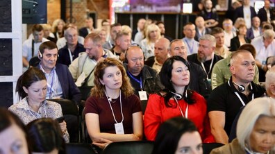 У залі сидять численні учасники Lviv Eco Forum 2026, та слухають виступ. На першому плані видно жінок і чоловіків з бейджами і навушниками для синхронного перекладу.