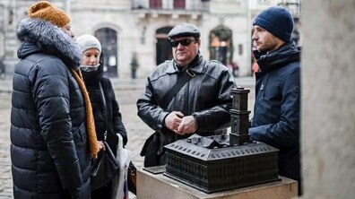 На площі Ринок у Львові група людей стоїть біля мініатюрного бронзового макета міської Ратуші, призначеного для тактильного ознайомлення з пам’яткою архітектури