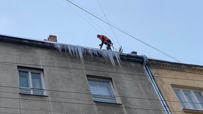 Альпініст у спецодязі на краю даху будинку збиває величезні бурулі