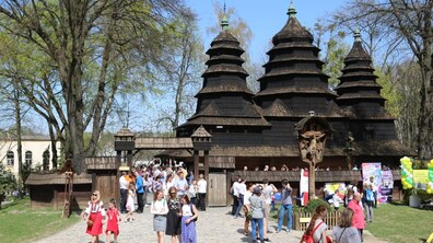 Перед старовинним дерев'яним храмом Премудрості Божої, що на території музею, ходять відвідувачі. Позаду видно зелені дерева.