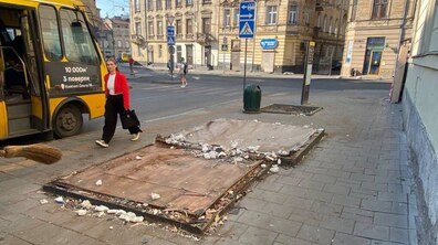 На тротуарі видно місце, де після демонтажу тимчасової споруди залишилася основа конструкції та будівельне сміття. На задньому плані вулиця з пішоходами