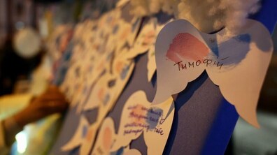 На великій синій дошці почеплені паперові ангелики. На передньому плані – ангелик із синьо-рожевими крилами, на якому написано ім’я «Тимофій». Фото архівне, з минулих таких акцій на площі Ангелів.