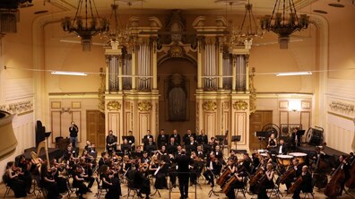 На фото зображено великий симфонічний оркестр, що виступає в просторій концертній залі з класичним інтер'єром. За сценою розміщений великий концертний орган. Фото ілюстративне.
