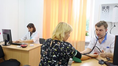 Медичний працівник вимірює тиск у пацієнтки. Трішки далі за комп’ютером сидить ще одна медична працівниця. Фото ілюстративне.