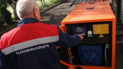 Фото ілюстративне. Працівник «Львівтеплоенерго» у спецодязі налаштовує великий помаранчевий генератор на вулиці, натискаючи кнопки на його панелі керування.