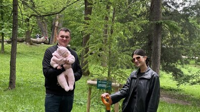 батьки з немовлям на руках біля висадженого дерева в парку міста
