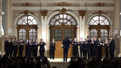 Учасники хору “Гомін” у чорних костюмах виступають на сцені Органного залу. Диригент хору Вадим Яценко стоїть спиною до глядачів, керуючи співом артистів перед повною залою слухачів.