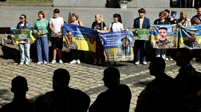 Акція - Учасники пам’ятної акції з плакатами та банерами із фотографіями українських військових, зниклих безвісти та полонених захисників. На передньому плані видно силуети присутніх, які спостерігають за заходом. Фото: Роман Балук