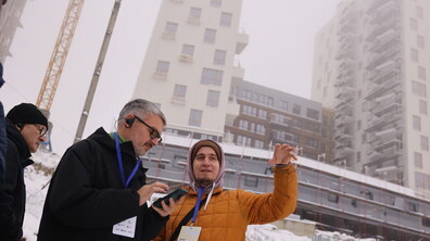 Представники команд міжнародних та українських фахівців з архітектури та містопланування під час екскурсії на території північного Львова. Позаду двох чоловіків, які спілкуються, зводять багатоповерховий будинок. Земля вкрита снігом