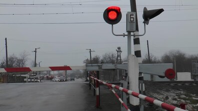 Залізничний переїзд, перекритий опущеним шлагбаумом із червоно-білими смугами. Перед шлагбаумом увімкнений червоний сигнальний ліхтар, що забороняє рух транспорту. Поруч видно металеву опору зі світлофором