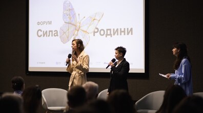На фоні великого екрана, де написана назва форуму «Сила родини», учасники і організатори стоять з мікрофонами в руках і спілкуються з присутніми. у залі люди слухають лекцію