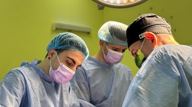 троє лікарів оперують пацієнта, лікарі одягнені у медичні халати, шапочки та маски