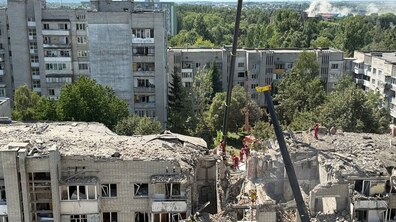 Частина багатоповерхівки майже повністю знищена: обвалені перекриття та стіни, вибиті вікна, навколо — уламки бетону й цегли. На місці працюють рятувальники та важка техніка, розбираючи завали.