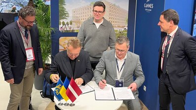 Мер Львова Андрій Садовий та мер Риги Вієстурс Кляйнбергс підписують Меморандум про співпрацю за столом на міжнародній виставці у Каннах. На столі прапорці Львова, України та Литвії. Довкола стоять партнери. Позаду на стенді візуалізації хірургічного корпусу лікарні св. Пантелеймона