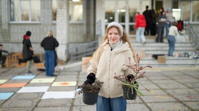 дівчина перед школою тримає в руках вазони для висадки на клумбі