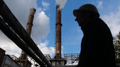 На фото — силует працівника теплоенергетичного підприємства на тлі промислових труб котельні, з яких у небо підіймається пара