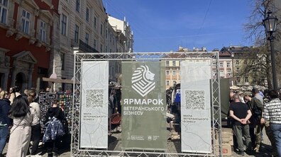 Група людей стоїть на площі Ринок біля стенду із написом «Ярмарок ветеранського бізнесу», а довкола - торгові ятки та відвідувачі