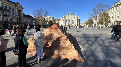 Діти розглядають мистецький об’єкт «Говерла». Це піраміда, складена із червоної цегли на площі перед Оперним театром у Львові. Навколо багато людей, поруч – старовинні будинки.