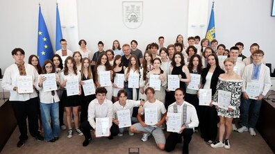 У сесійній залі на фоні державного прапора та прапора Євросоюзу школярі і школярки у святковому вбранні показують вручені нагороди