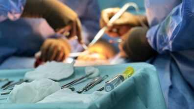 Операційна під час хірургічного втручання. Медичні працівники у стерильних халатах і рукавичках працюють із хірургічними інструментами над пацієнтом, який лежить під яскравим операційним світлом. На передньому плані розкладені інструменти та шприц, підготовлені для процедури.