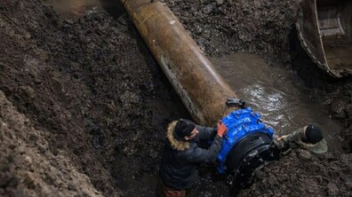 Глибока яма у якій два працівники Львівводоканалу монтують нову трубу великого діаметру. Праворуч у ямі видно ківш екскаватора.