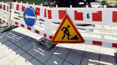 Фото ілюстративне. На вулиці стоїть біло-червона огорожа, на якій розміщені дорожні знаки: синій зі стрілкою вліво та жовтий трикутний «Дорожні роботи».