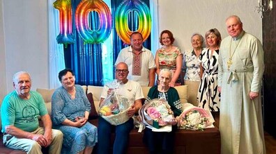 Родинне святкування з нагоди 100-річного ювілею. Ювілярка пані Ганна сидить серед рідних та близьких і тримає в руках букети квітів. Позаду є святкові повітряні кульки з цифрою «100». Усі присутні дивляться в камеру й усміхаються.