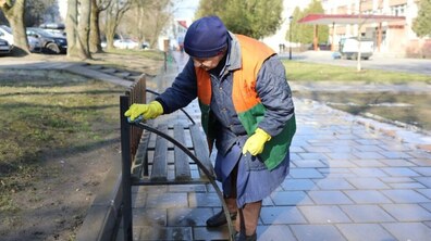 двірниця миє лавку, яка стоїть на алеї