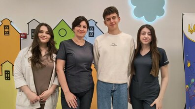 У холі дитячої лікарні святого Миколая пацієнт Дмитро та медичні працівниці стоять один біля одного та усміхаються, дивлячись в камеру.