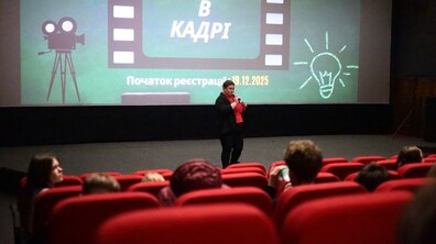 На сцені жінка говорить у мікрофон у кінотеатрі. На екрані позаду напис “Освіта в кадрі”.