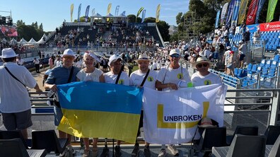 Команда гравців стоїть на трибунах. Учасники змагань тримають у руках український прапор та стяг з логотипом львівського центру UNBROKEN. Довкола них багато глядачів