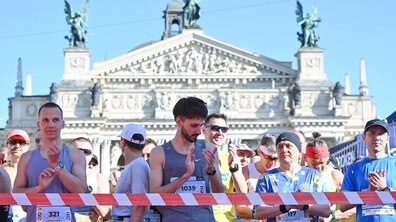 Учасники забігу у спортивній формі стоять за сигнальною стрічкою перед забігом. Позаду них видно будівлю Львівського національного театру опери та балету імені Соломії Крушельницької