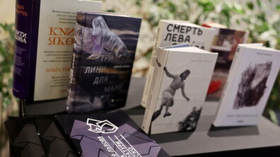 На темному столі розставлені сучасні українські видання, що були представлені на премії Львова — міста літератури ЮНЕСКО. Серед них виділяється книга Сергія Осоки «Три лини для Марії» з ілюстрацією риби на обкладинці та книга Ірини Шувалової «Каміньсадліс». Перед книжками лежать інформаційні буклети премії з геометричним фіолетовим візерунком