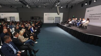 На сцені сидять спікери і спілкуються з слухачами у великому залі. На стінах напис –