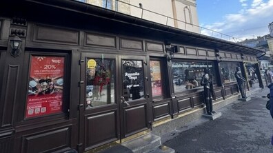 Довга одноповерхова будівля з дерев'яним коричневим фасадом закритого літнього майданчика, в якому працює ресторан. На вхідних дверях напис «Язиката теща». Поруч статуї лицарів в обладунках
