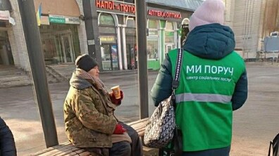 соціальна працівниця «Джерела» розмовляє з жінкою на зупинці громадського транспорту.