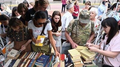 Люди розглядають і вибирають книги на вуличному книжкообміні. Біля столу, заповненого виданнями різних форматів і кольорів, зібралися відвідувачі різного віку, які розглядають книжки.