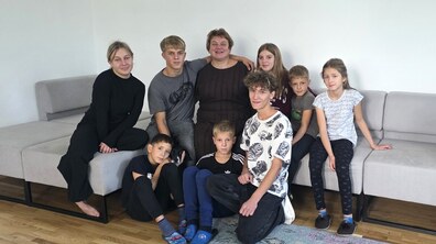 Спільне фото дітей та мами-виховательки Дитячого будинку сімейного типу. Усі сидять на дивані та біля нього у кімнаті, обіймаючи один одного та усміхаючись.