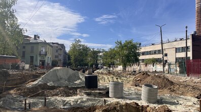масштабні ремонтні роботи на перехресті вул. Залізнична-Ясна. Видно розриту землю, купи піску та бетонні кільця для комунікацій. Ліворуч стоять світло-зелений будинок і дерева, праворуч — довга промислова будівля з високою трубою.