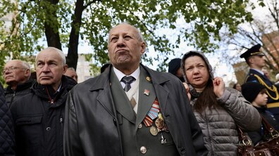 Група людей на вулиці під час урочистості з нагоди 40-х роковин аварії на Чорнобильській атомної електростанції. У центрі — літній чоловік із медалями на грудях, із серйозним виразом обличчя; поруч інші люди й військовий на задньому плані.