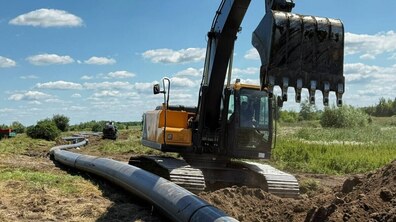 Роботи із заміни водопроводу на відкритій ділянці. На передньому плані стоїть великий гусеничний екскаватор із піднятим ковшем, а поруч тягнеться нова чорна поліетиленова труба великого діаметра.