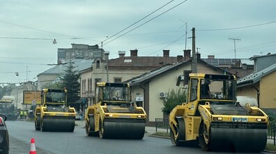 Ремонт вул. Городоцька. Дорогою в ряд рухаються три великі жовті дорожні котки, які ущільнюють щойно постелене асфальтне покриття. Попереду встановлено сигнальний конус, а вдалині видно працівників дорожньої служби та спецтехніку.