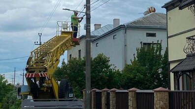 Біля приватних житлових будинків працівник у білій захисній касці на автовишці встановлює на ліхтарі освітлення