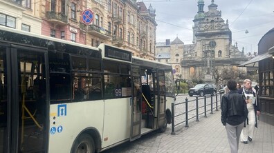 Міський автобус № 99 стоїть у центрі Львова, поруч проходять люди. На другому плані – старовинна архітектура, зокрема храм Святого Андрія