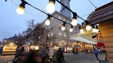 Вечірня площа Ринок у Львові з різдвяними дерев’яними будиночками ярмарку, гірляндами лампочок, фонтаном зі скульптурою в центрі та людьми, які повільно прогулюються бруківкою на тлі Ратуші