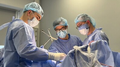 Троє лікарів у спеціальних медичних халатах, масках та шапочках оперують в операційній кімнаті. Фото ілюстративне