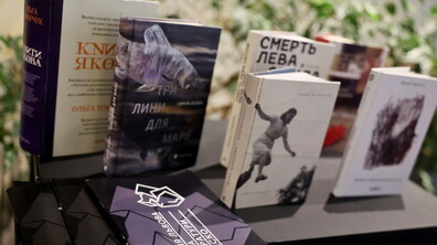 На темному столі розставлені сучасні українські видання, що були представлені на премії Львова — міста літератури ЮНЕСКО. Серед них виділяється книга Сергія Осоки «Три лини для Марії» з ілюстрацією риби на обкладинці та книга Ірини Шувалової «Каміньсадліс». Перед книжками лежать інформаційні буклети премії з геометричним фіолетовим візерунком