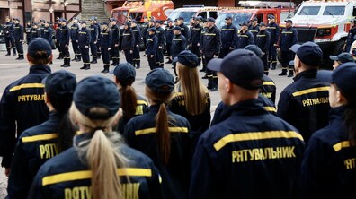 Урочистості з нагоди Дня рятівника: велика кількість рятівників у формі вишикувалися перед пожежно-рятувальною технікою. На задньому плані видно кілька пожежних та аварійно-рятувальних автомобілів. На темно-синій формі видно написи жовтими літерами: «РЯТУВАЛЬНИК».