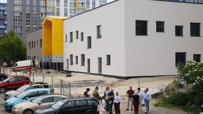 Двоповерхова будівля нової школи, будівництво якої перебуває на завершальному етапі. Великі панорамні вікна, а головний акцент – на вході, який забарвлений у яскраво-жовтий колір. На території тривають роботи з благоустрою. Хід виконання робіт оглядають міський голова, освітяни та забудовники
